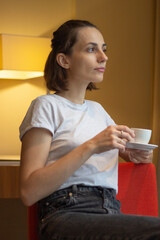 a girl sits sideways looking into the distance and drinks coffee from a cup