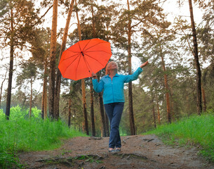 Happy mature woman with red umbrella enjoy in a forest under the rain