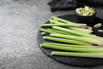 Slate board with fresh lemongrass stalks on grey table. Space for text