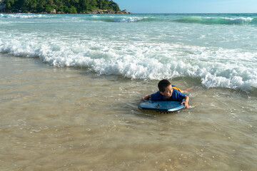 Fototapeta na wymiar The waves swept the surf boy toward the shore..boy surfing on white waves..Paradise beach blue sea, and clear sand landscape background..smiling face of happy boy surfing concept.