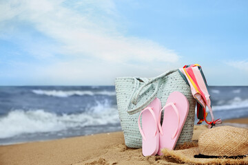Bag and different beach objects on sand near sea, space for text