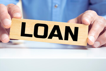 Cropped view of hands holding wooden block with LOAN lettering on work table.