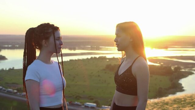 Two young women talking on a background of sunset field and river
