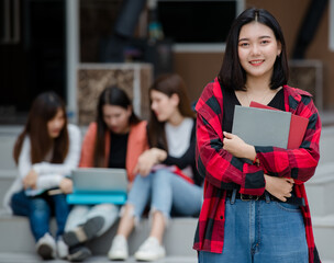 Close up young attractive female college students holding document files smiling at camera with blurry university campus and other students. Outdoor. Concept for education, college students life
