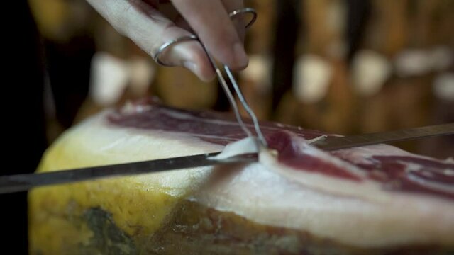 Closeup of man carving thin slice of traditional Serrano dry-cured Ham