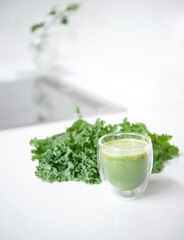 Kale smoothie in glass and kale leaves isolated on mable countertop. Healthy food concept