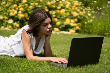 A young girl in a white dress is working on a laptop.