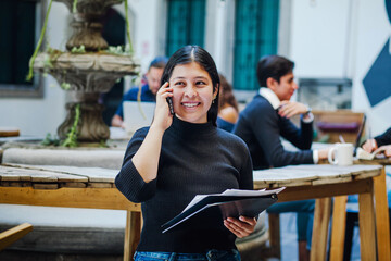 Portrait of young latin student girl talking on phone in college in Mexico City