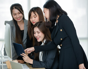 Group of four attractive Asian female office colleagues in formal business suits looking at ipad...