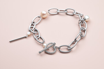 Steel chain bracelet with pearls pendant on pastel pink background
