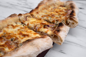 Italian cuisine. Selective focus on a sliced mozzarella cheese pizza with onion and different kinds of cheese on the white marble table.