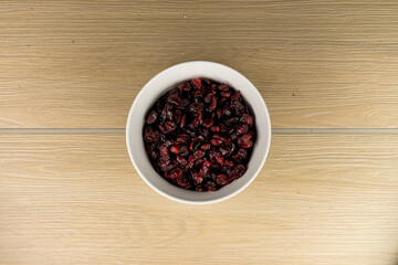 Tazón de cerámica blanca con arándanos secos sobre madera