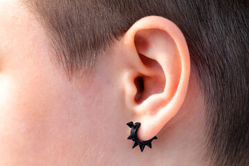 Black earring in the ear close-up, ear piercing