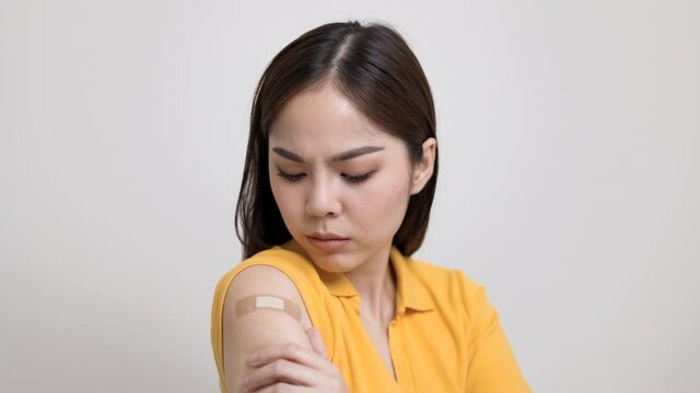 Young beautiful asian woman in yellow shirt feel pain in arm after receiving the vaccine. She was worried and stressed that there would be side effects. She tried to massage her aching arm.