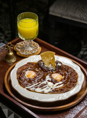 Desayuno especial de huevos rancheros con mole poblano y frijoles refritos sobre plato blanco y jugo de naranja.