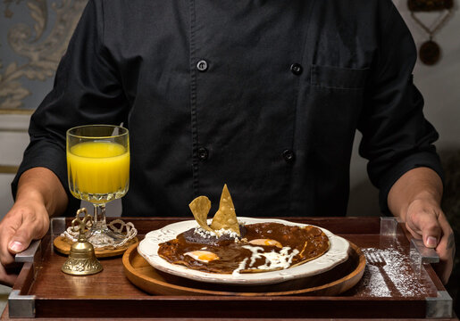 Desayuno especial de huevos rancheros con mole poblano y frijoles refritos sobre plato blanco y jugo de naranja.