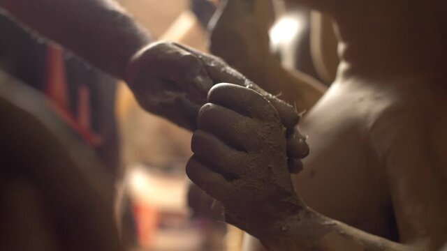 Indian artist shaping the hand of unfinished clay sculpture in his craft factory. Closeup shot of craftsman's hand making statues of different deities for the Durga Puja festival celebrated in India