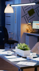 Interior of professional empty start-up business office meeting room with nobody in it. On table standing financial documents late at night. In background computer with company graph on monitor