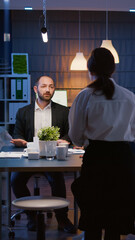 Diverse teamwork overworking in meeting room planning company strategy analyzing management statistics late at night. Multi ethnic coworkers sitting at conference table solving financial presentation