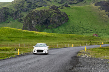 White cars run on asphalt roads in Icelandic countryside, mountains green grass and summer looks fresh and bright, holiday driving trips.