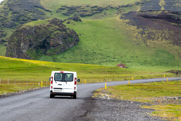 White cars run on asphalt roads in Icelandic countryside, mountains green grass and summer looks fresh and bright, holiday driving trips.