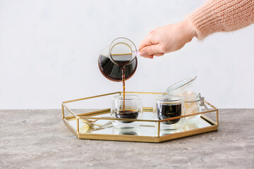 Woman pouring turkish coffee from cezve into cups in kitchen