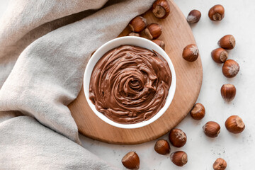 Bowl with tasty chocolate paste and hazelnuts on light background