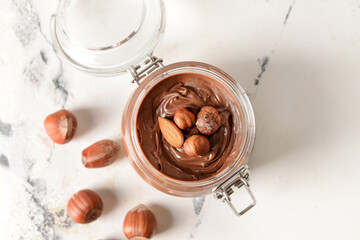 Jar with tasty chocolate paste and hazelnuts on light background