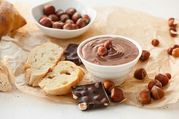 Bowl with tasty chocolate paste and hazelnuts on light background