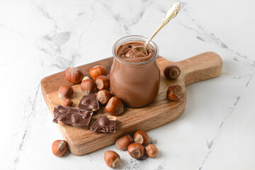 Jar with tasty chocolate paste and hazelnuts on light background