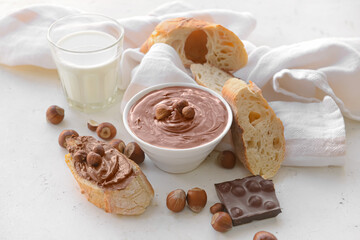 Bowl with tasty chocolate paste and hazelnuts on light background