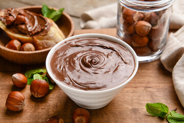 Bowl with tasty chocolate paste and hazelnuts on wooden background