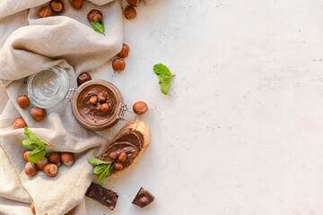 Jar with tasty chocolate paste and hazelnuts on light background