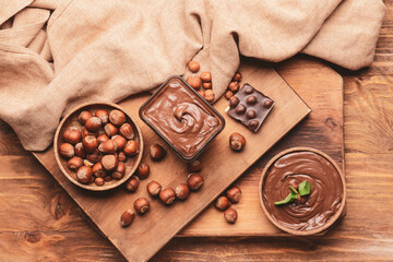 Bowl with tasty chocolate paste and hazelnuts on wooden background