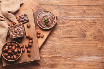 Fototapeta na wymiar Bowl with tasty chocolate paste and hazelnuts on wooden background