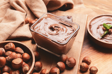 Bowl with tasty chocolate paste and hazelnuts on wooden background