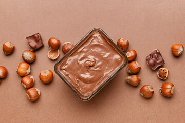 Bowl with tasty chocolate paste and hazelnuts on color background