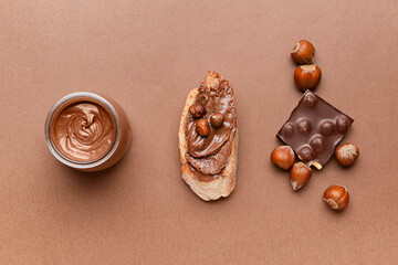 Jar and bread with tasty chocolate paste and hazelnuts on color background