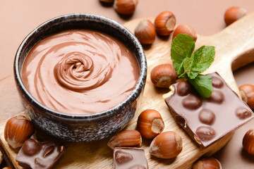 Bowl with tasty chocolate paste and hazelnuts on color background