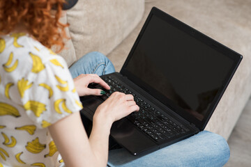 The redhead girl using a laptop. Back view. Work at home