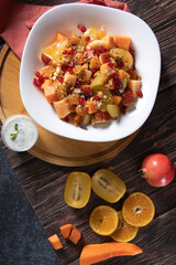 Organic vegan Fruit salad of papaya apple kiwi banana pomegranate raisins for healthy lifestyle dressed up in a bowl on chopping board