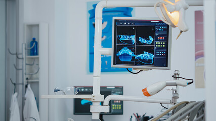 Close up revealing shot of medical stomatology display with x ray images on it. Empty professional hospital stomatology chair with nobody in it. Modern dentist equipment with dentistry tools