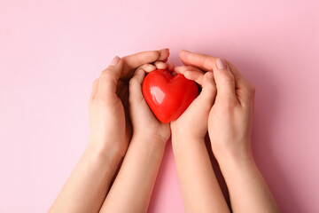 Hands of woman and child with red heart on color background