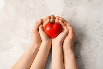 Hands of woman and child with red heart on grunge background