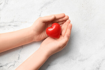 Child's hands with red heart on light background