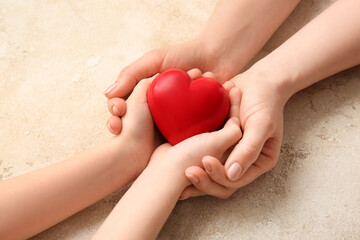 Hands of woman and child with red heart on grunge background
