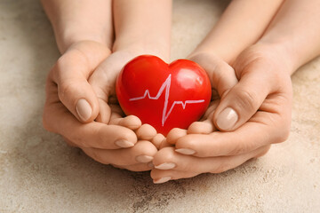 Hands of woman and child with red heart on grunge background, closeup