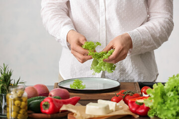 Woman preparing tasty Greek salad in kitchen