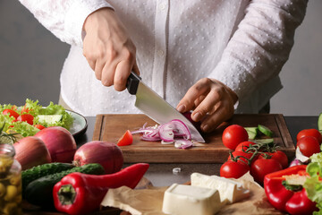 Woman cutting onion for tasty Greek salad on table