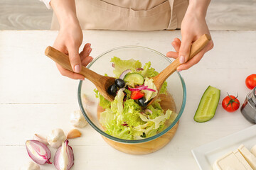 Woman preparing tasty Greek salad in kitchen
